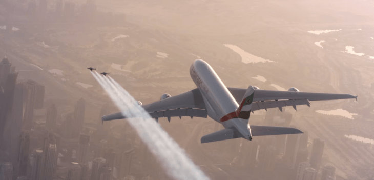 Two guys wearing jetpacks fly alongside an Airbus A380